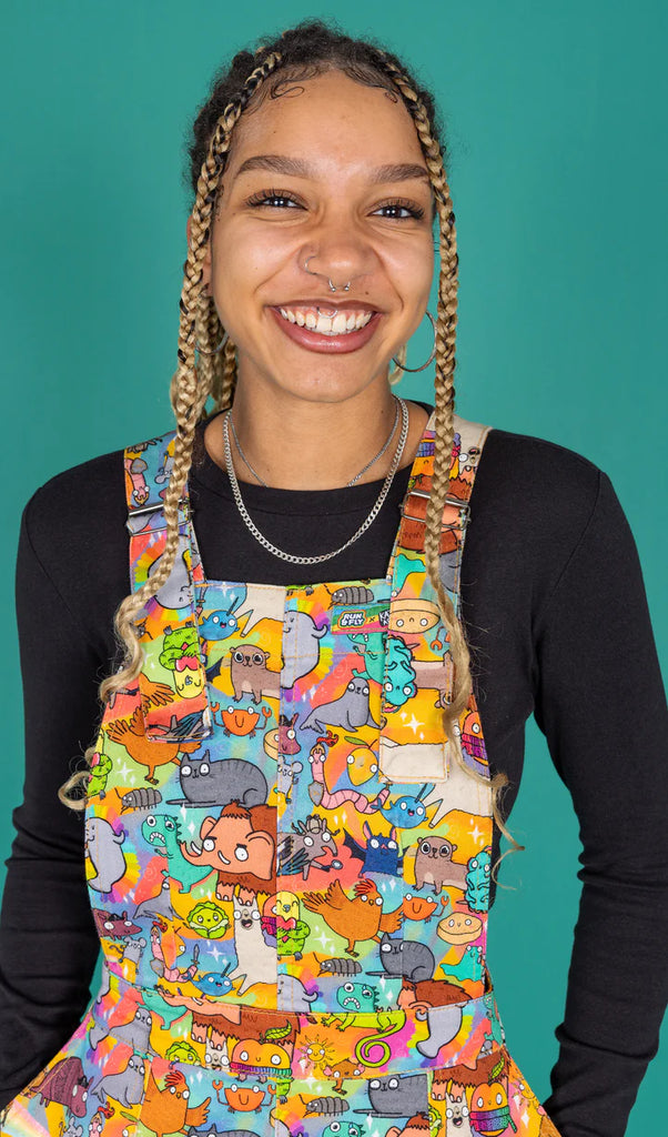 Close up of the front of this cute Run and Fly pinafore dress which is covered in and all over print of Katie Abey's designs. Characters include cats, bats, mamoths, otters, crumpets, lemons and more!